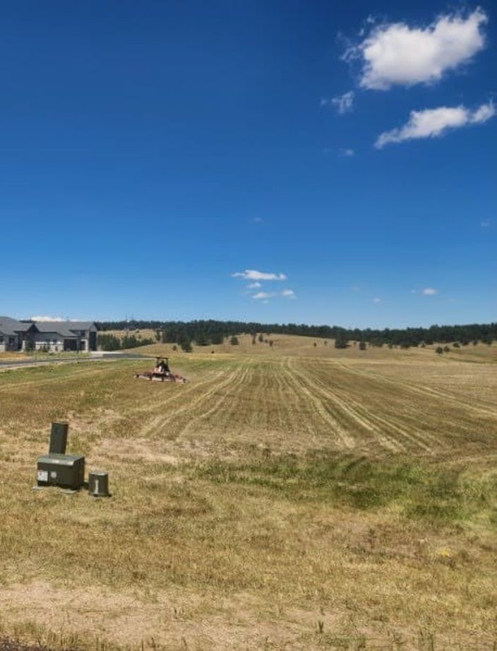 Tractor mowing a large native grass field with the Front Range on the horizon