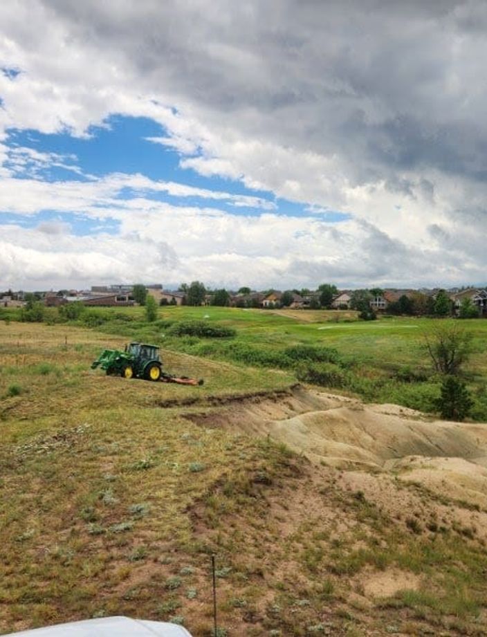 Tractor mowing native grass along a drainage swale beside a golf course