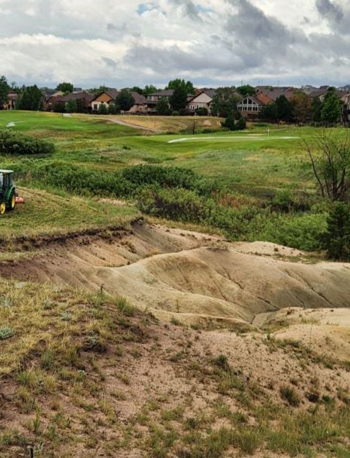 Tractor mowing right up to the edge of an eroded drainage on a Colorado Springs property