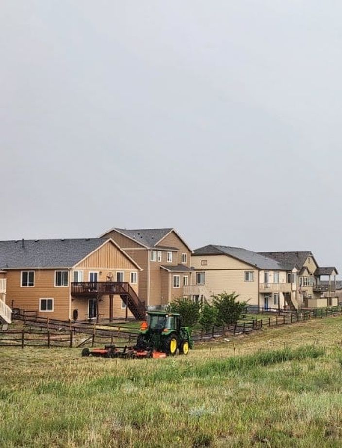 Tractor mowing the native grass fence line directly behind a row of Colorado Springs homes