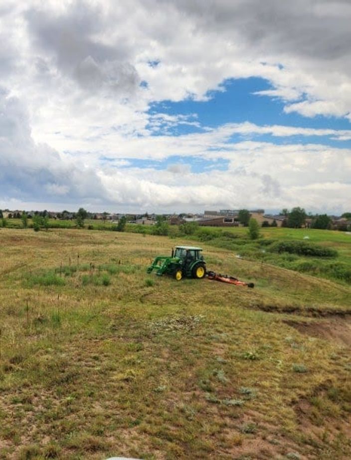 A&R tractor and rotary mower cutting native grass as storm clouds build over the Front Range