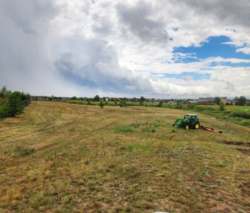 A&R tractor and rotary mower cutting native grass as storm clouds build over the Front Range
